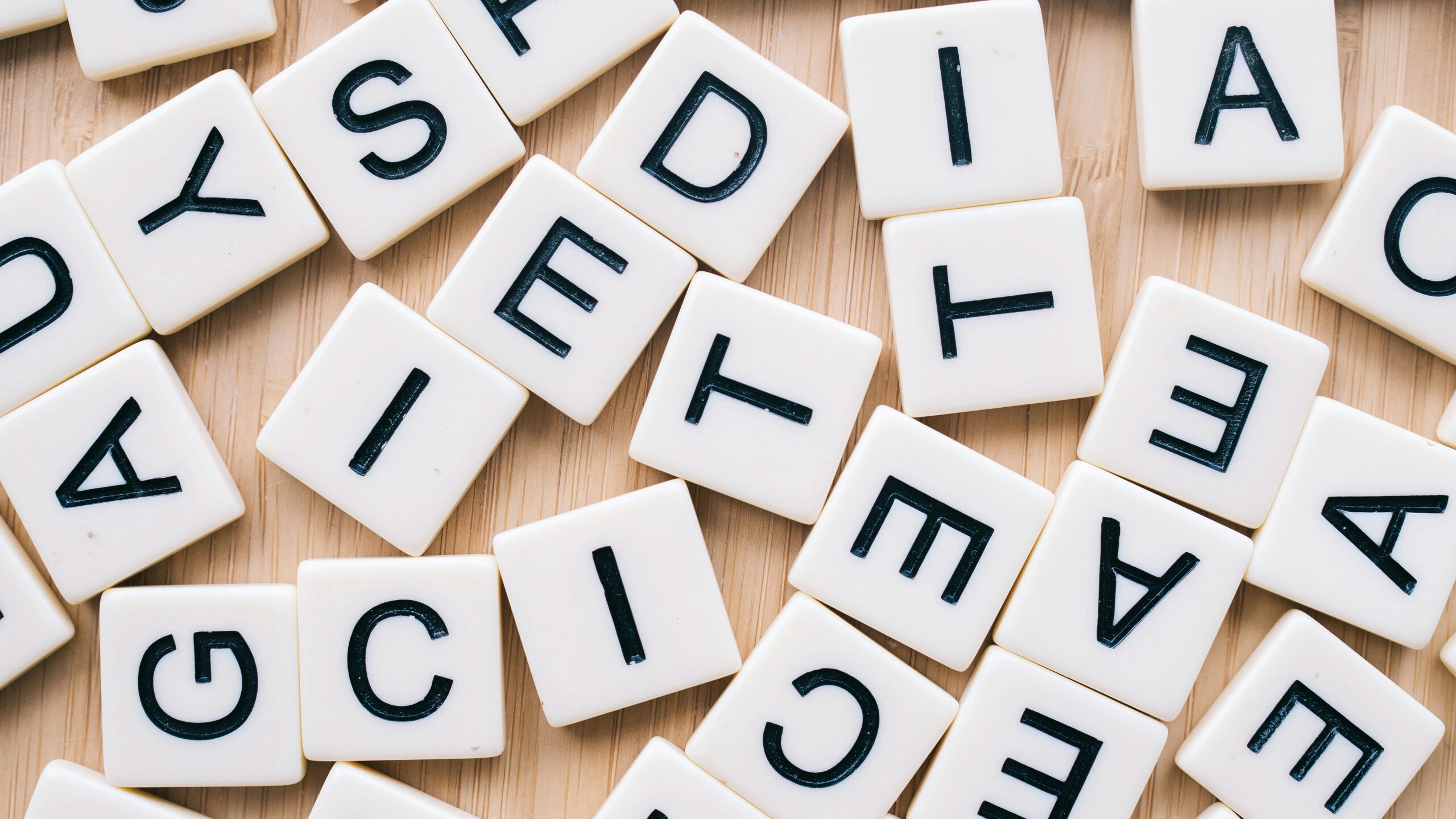 Closeup of scattered scrabble tiles against a wooden background, ideal for word games and learning themes.